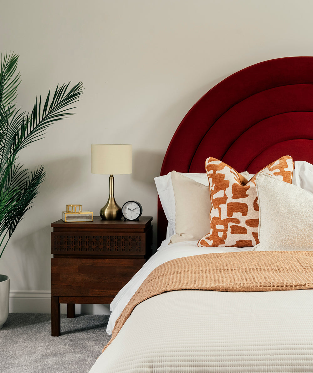 Cozy bedroom with a bold red headboard, patterned pillows, wooden nightstand, and neutral bedding.