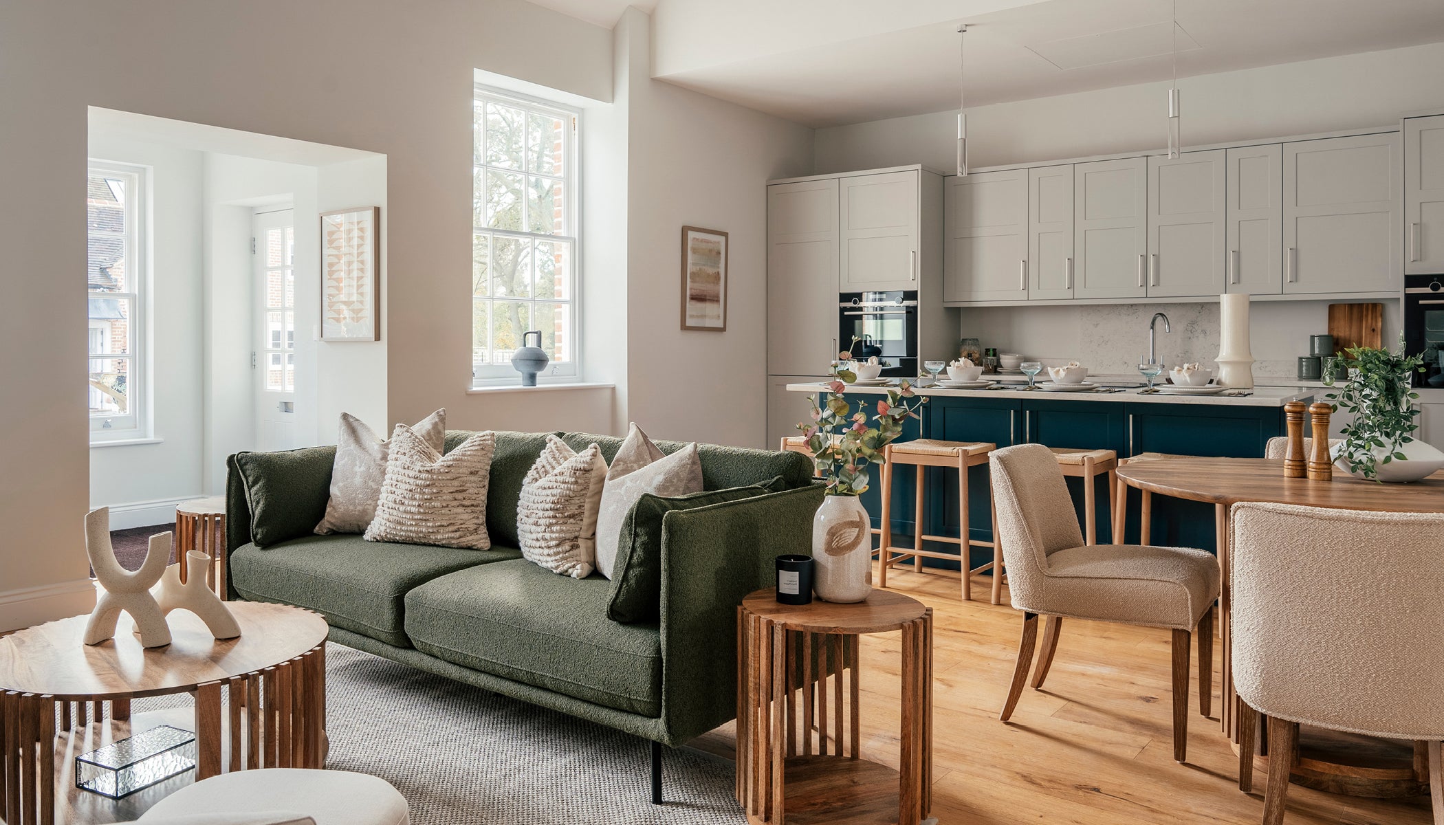 Open-plan kitchen and living area with a green sofa, wood-accented furniture, and a modern kitchen featuring white cabinets and a navy island.