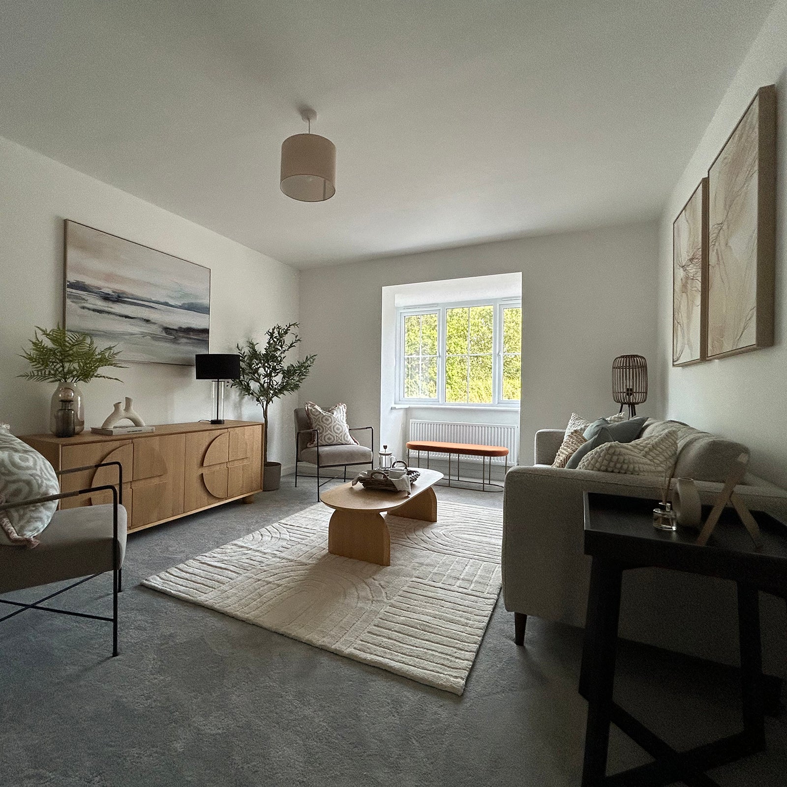 A cozy, modern living room featuring neutral-toned furniture, a wooden coffee table, large window, and minimalist decor with plants and abstract art.