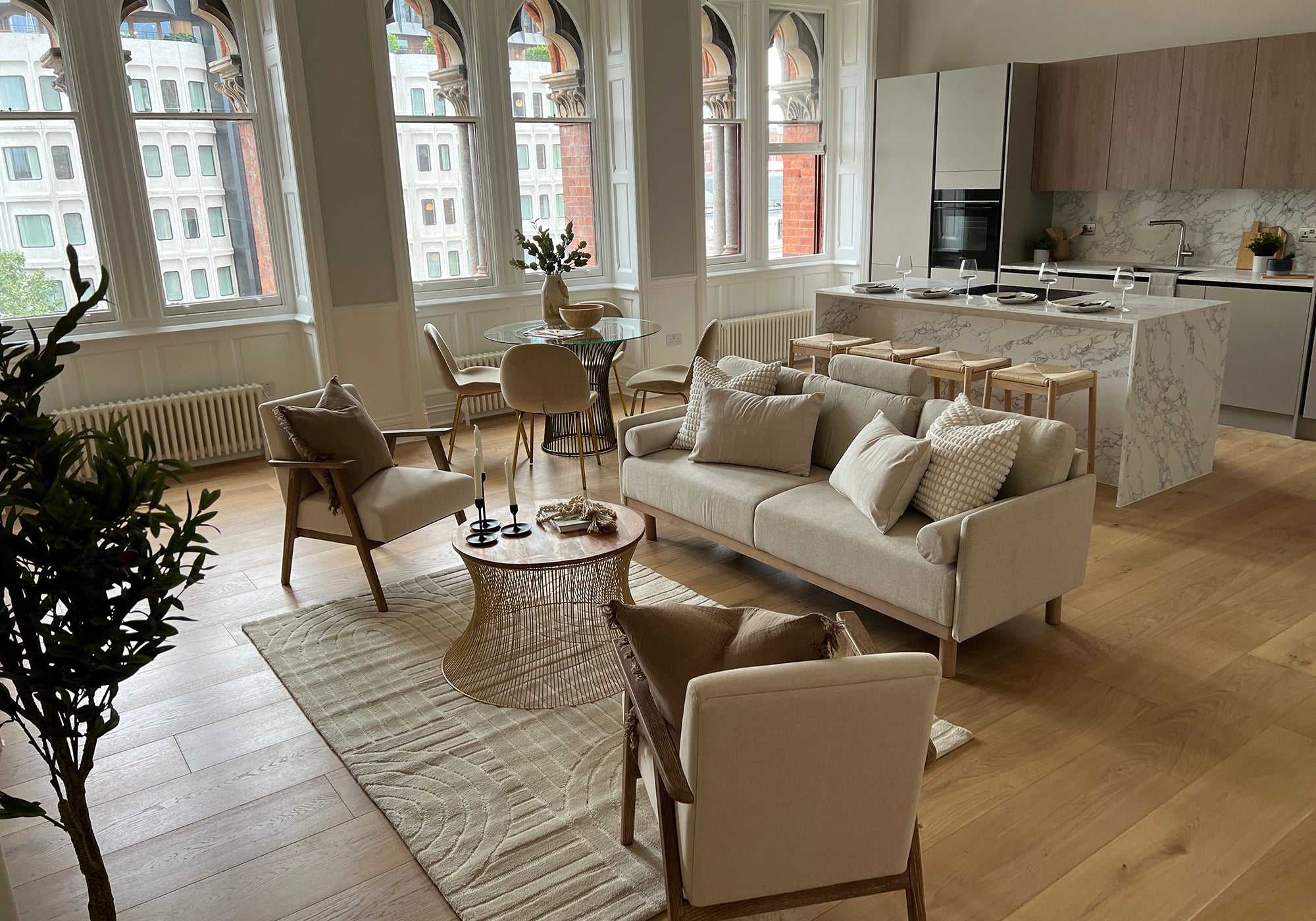 Neutral-toned open-plan living area with modern furniture, marble kitchen island, and large arched windows letting in natural light.