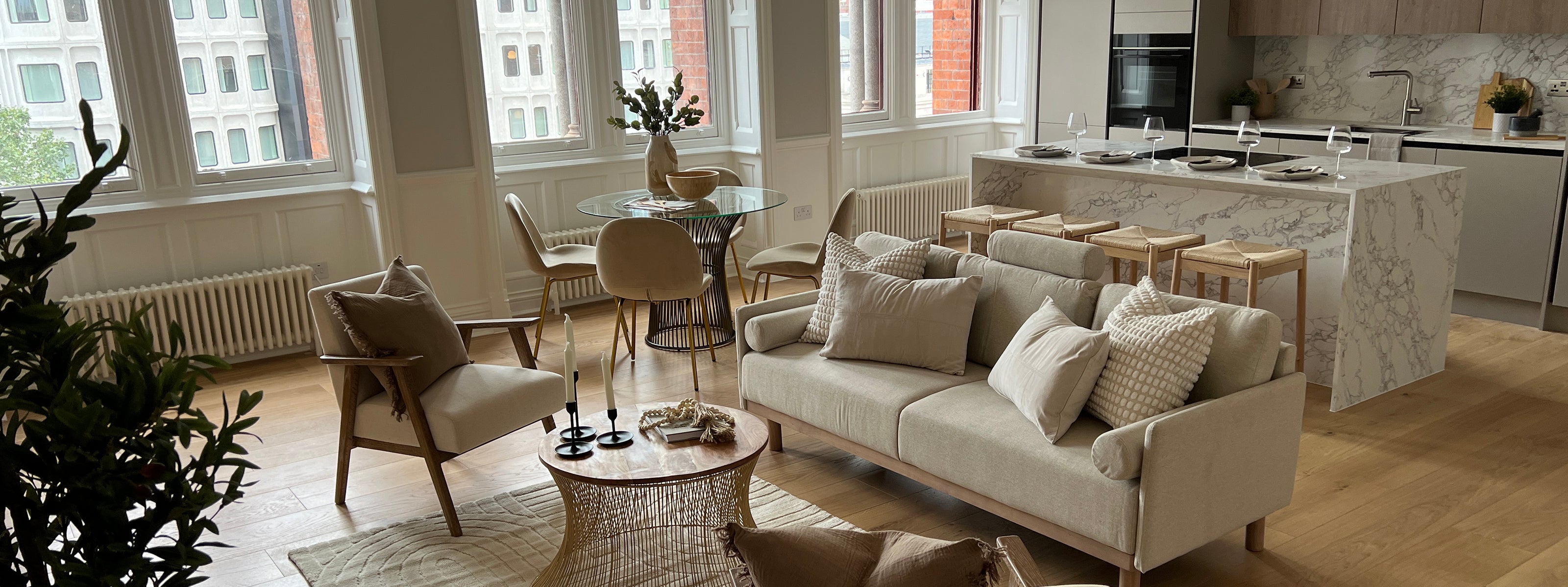 Modern open-plan living space with neutral furniture, a marble kitchen island, and large arched windows.